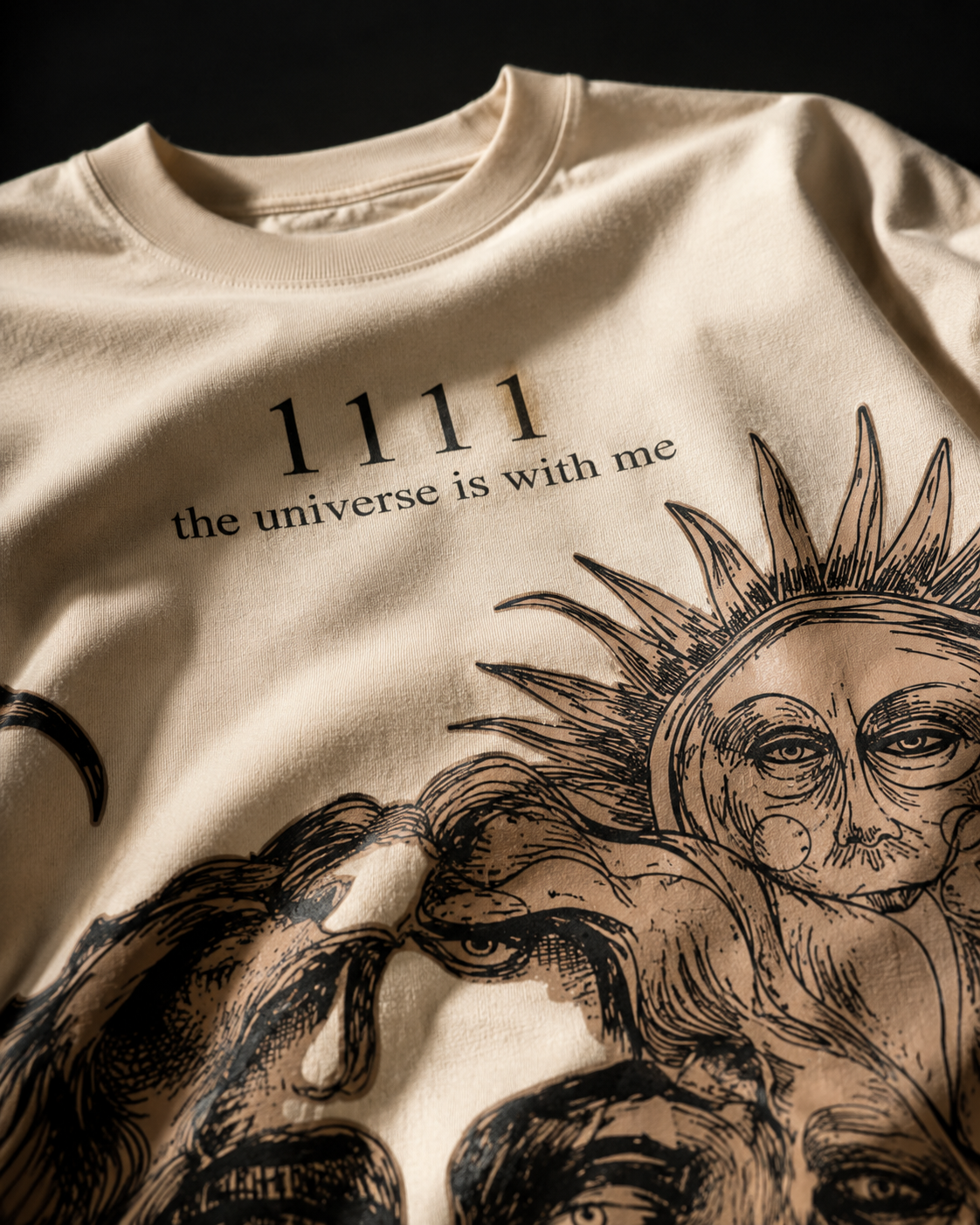 Close-up of the fine-line sun graphic and 1111 lettering printed on the cream cotton of the Manifest tee