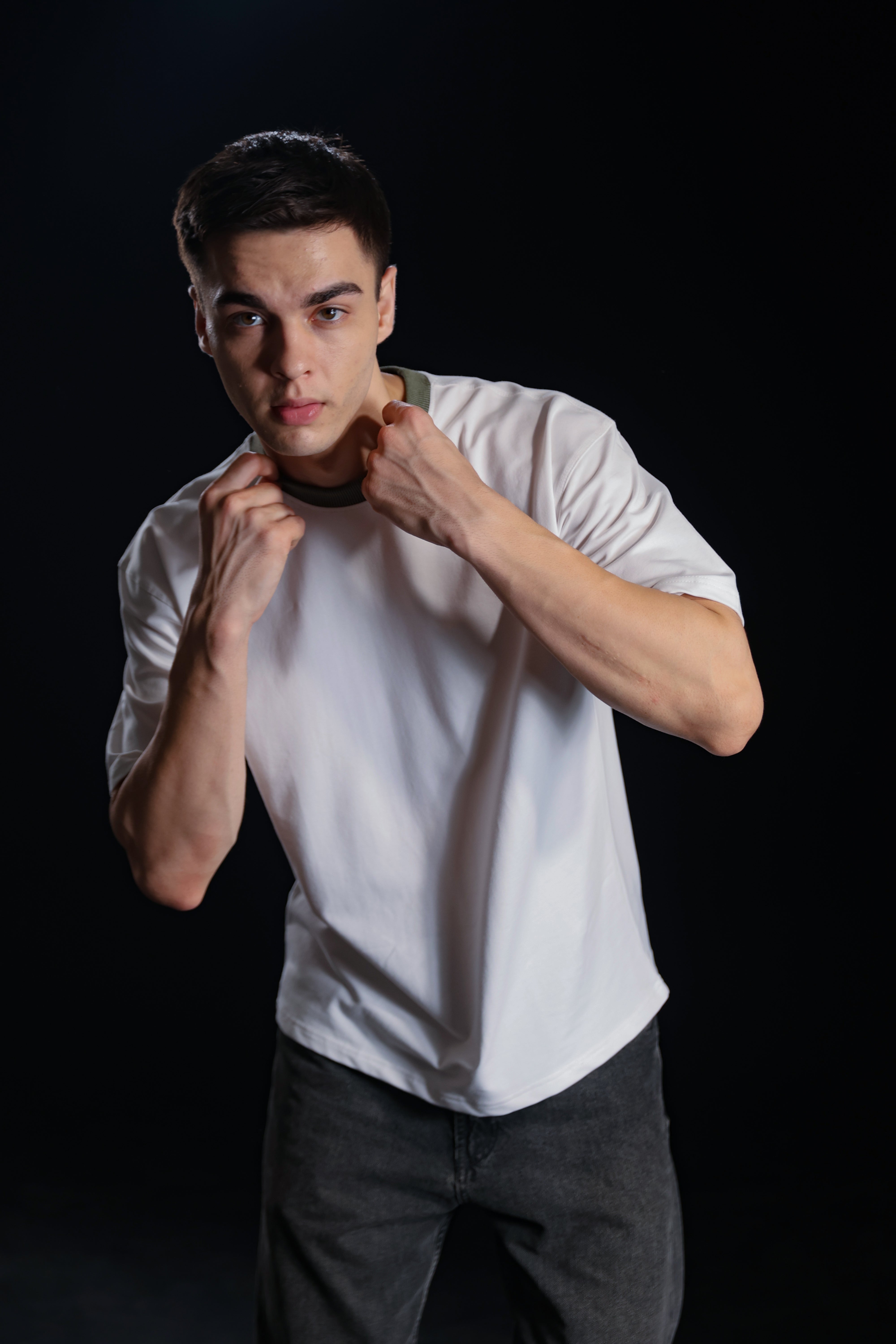 Man in a white t-shirt and dark pants posing with fists up on a black background