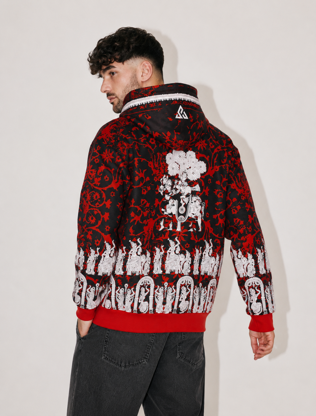 A man wearing a black and red patterned hooded sweatshirt with white graphic prints, shown from the back against a plain light background.