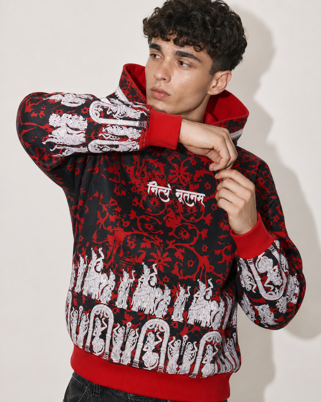 A man wearing a black and red patterned hoodie with white graphic prints and red cuffs, collar, and hem, posed against a plain light background.