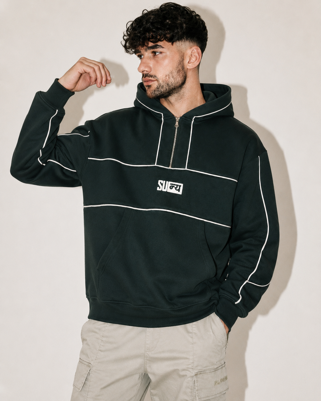 A man wearing a dark green pullover hoodie with white piping and a white chest logo that reads 'SJ FZ', paired with light beige cargo pants, posing against a plain off-white background.