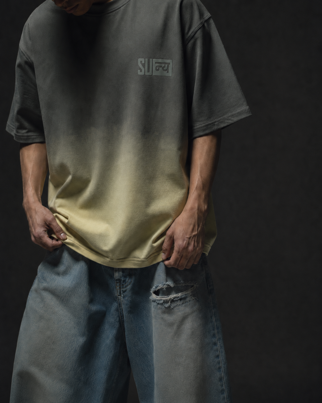 Ombrix tee in olive fading to sage — torso and hem view, model holding the hem above distressed jeans