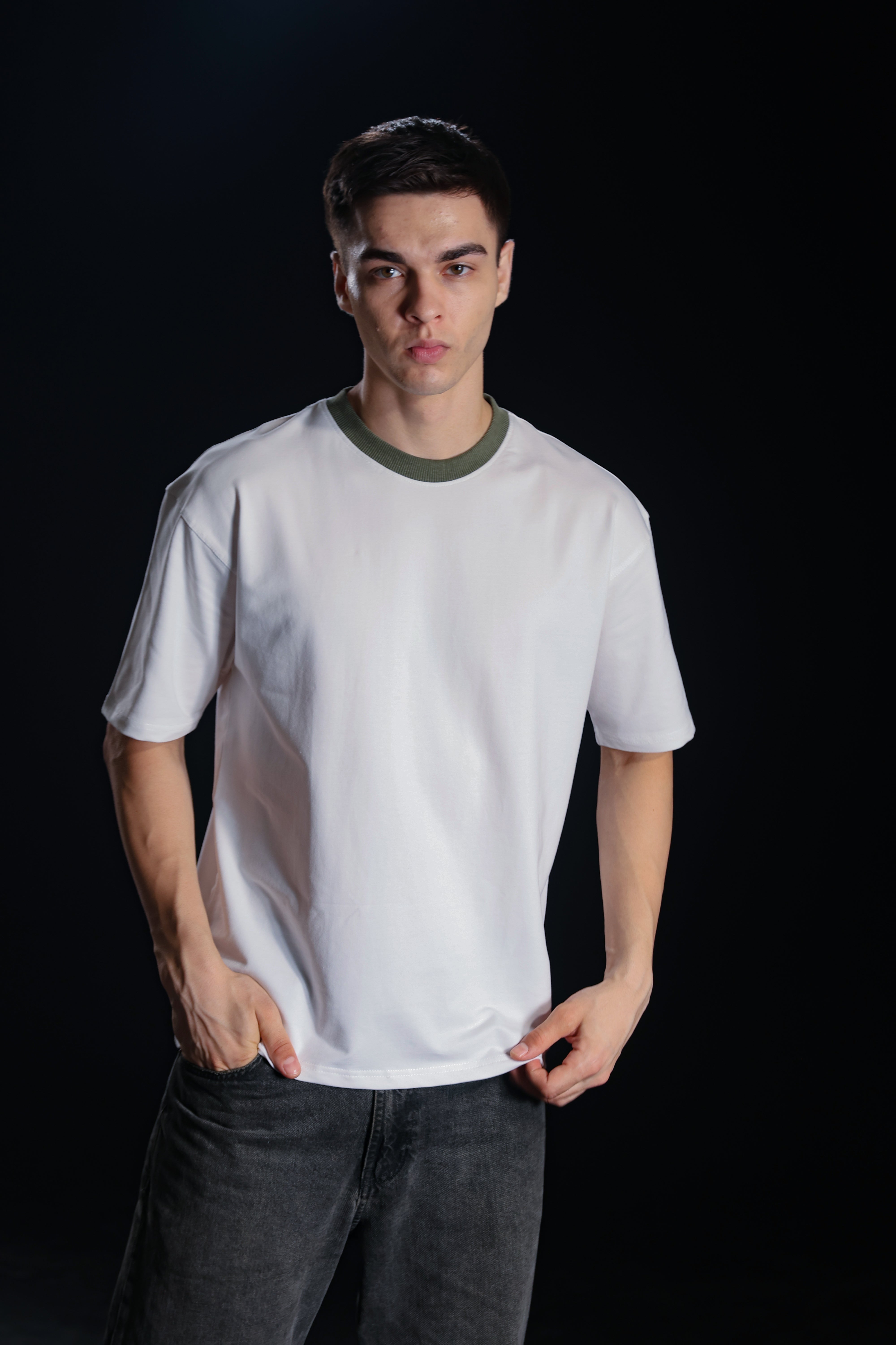 Person wearing a plain white t-shirt with green trim on a black background