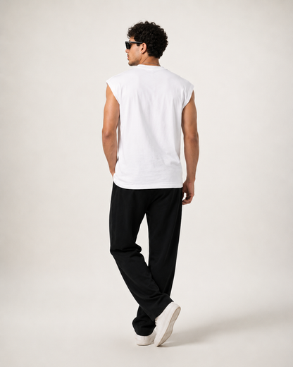 A man shown from the back wearing a white sleeveless t-shirt, black pants, and white sneakers against a plain light gray studio background.