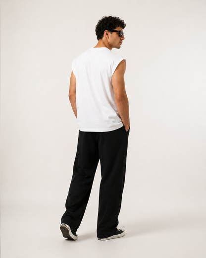 A man wearing a white sleeveless t-shirt and black pants, shown from a rear three-quarter view against a plain light gray studio background.