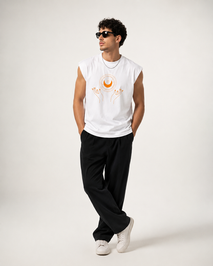 A man modeling a sleeveless white t-shirt with a celestial graphic, paired with black pants and white sneakers, against a plain light gray background.