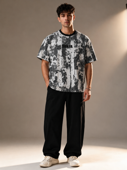 A man modeling a black and white abstract patterned t-shirt with 'BENITA' printed across the chest, paired with black sweatpants and white sneakers, set against a warm beige studio backdrop.
