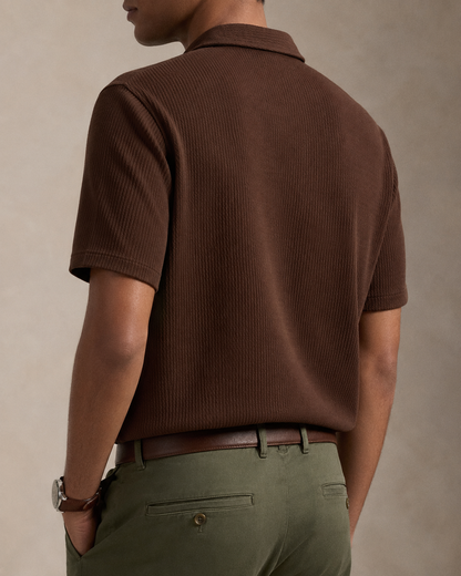 A man shown from the back wearing a brown short-sleeve ribbed knit polo shirt and olive green trousers, against a neutral textured beige background.