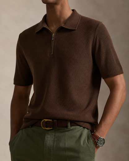 A man wearing a brown ribbed short-sleeve polo shirt with a half-zip collar, styled with olive green trousers and a brown belt.