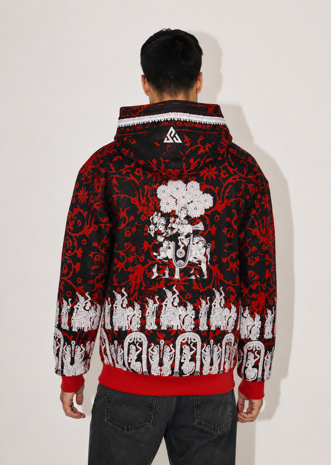 A man viewed from behind wearing a black and red hooded jacket with a white graphic print on the back, paired with dark gray jeans, against a plain off-white background.
