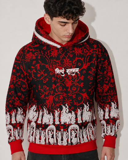 A man wearing a black and red patterned hoodie with white script on the chest and a white graphic border along the hem, photographed against a plain light background.