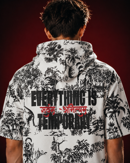 A man viewed from behind wearing a white short-sleeve hoodie with a black tropical jungle print and bold text on the back reading 'EVERYTHING IS TEMPORARY' with red script in the middle, against a dark red background.