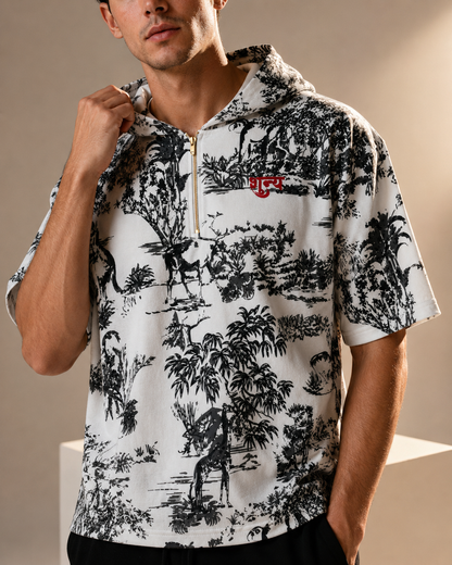 A man wearing a short-sleeve half-zip hoodie with a black and white toile de Jouy print and a small red embroidered tiger logo on the chest.