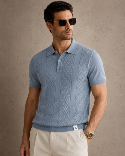 CORD knit polo in slate — front view on model against a plaster wall, styled with cream trousers