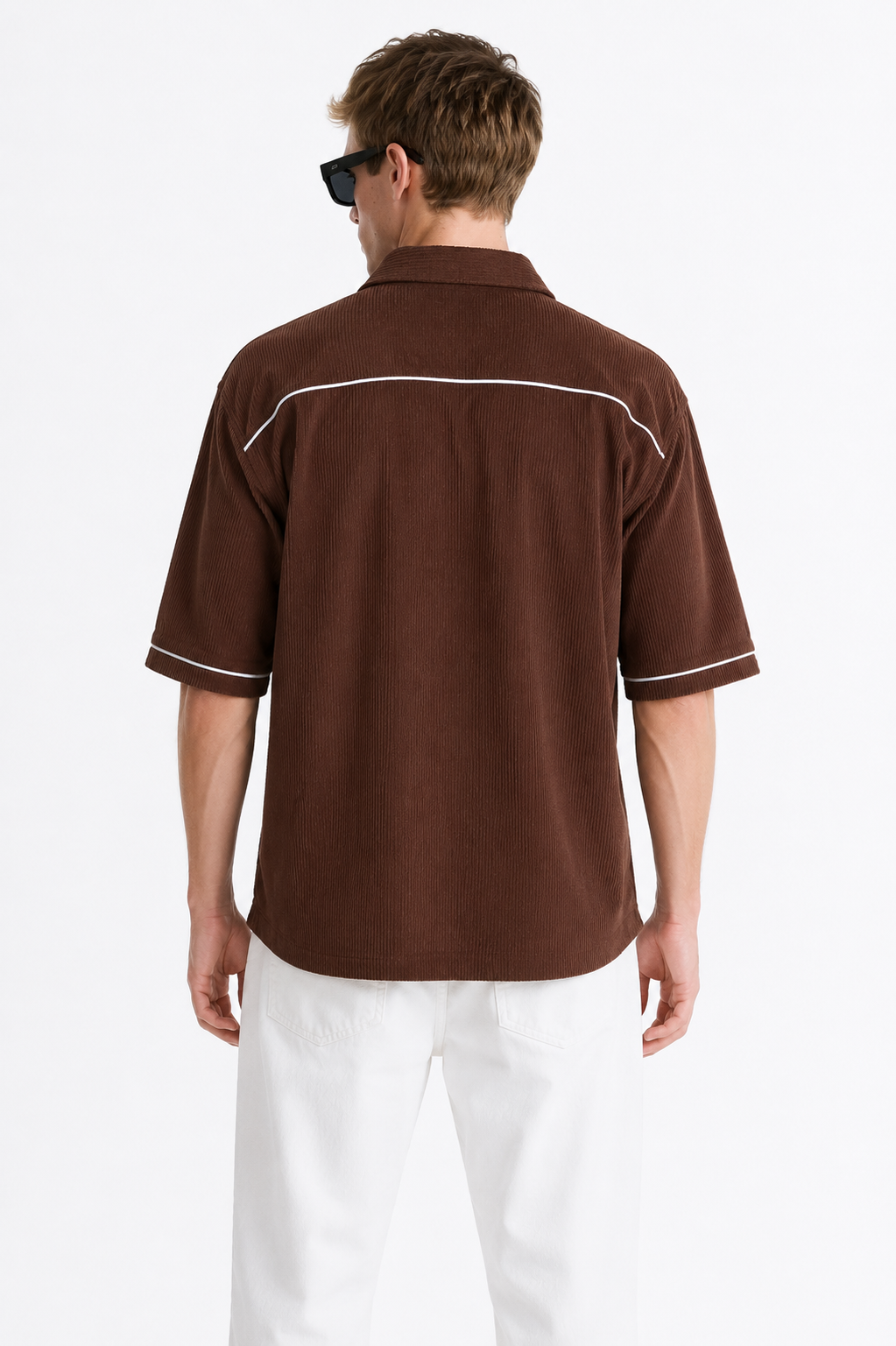 A man viewed from the back wearing a brown short-sleeve button-up shirt with white contrast piping and white pants, against a plain light background.