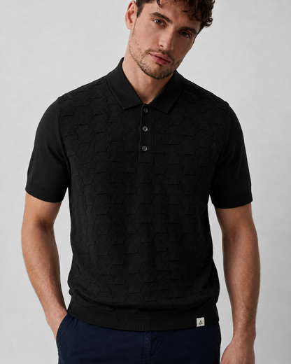 LEAF Knit Polo in black — on model over navy trousers, woven tab at the ribbed hem, hands in pockets