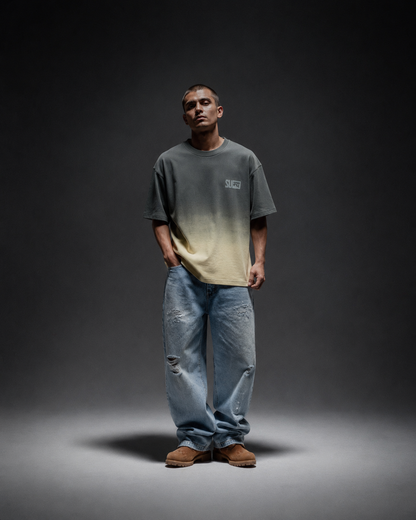 Ombrix tee in olive fading to sage — front view on model with hands drawn behind, spotlit on a dark set
