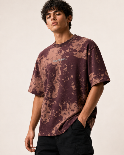 A man wearing a short-sleeve crewneck t-shirt with a brown and beige abstract pattern and 'Maison Michel' text on the chest, paired with black pants, against a plain light background.