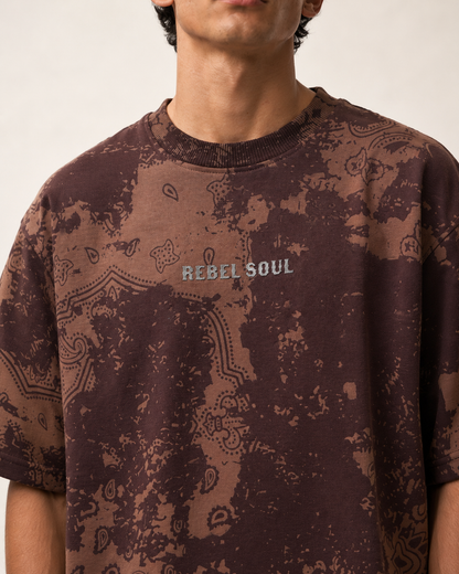 A close-up of a person wearing a brown and dark brown acid-wash t-shirt with a paisley pattern and 'REBEL SOUL' printed on the chest.