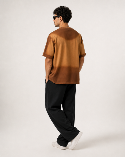 A man wearing a brown short-sleeve t-shirt with a gradient design, black pants, and white sneakers, photographed from the back against a plain light gray studio background.
