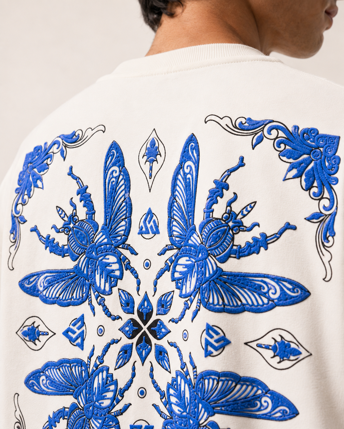 Close-up of the back of a white crewneck sweatshirt featuring a large, detailed blue embroidered butterfly and floral pattern, worn by a model.