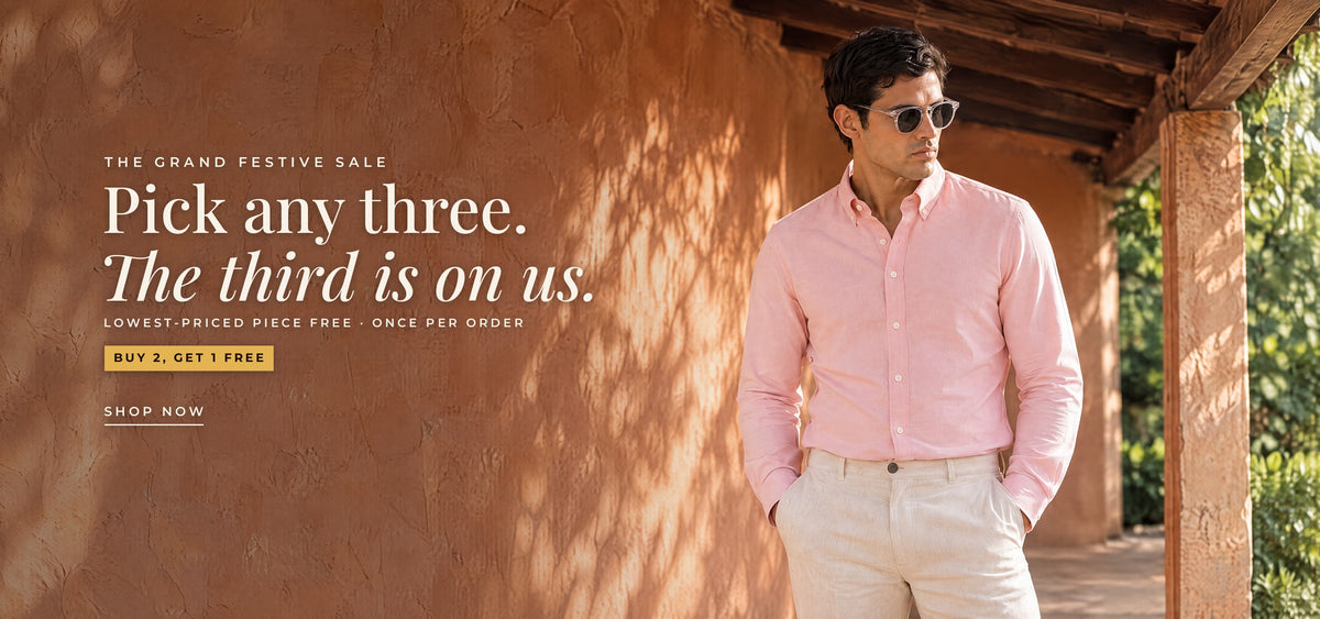 The Grand Festive Sale: pick any three, the third is on us. Buy 2, Get 1 Free, lowest-priced piece free, once per order. A man in the Blush Oxford shirt and clear-frame sunglasses by a terracotta wall. Shop now.
