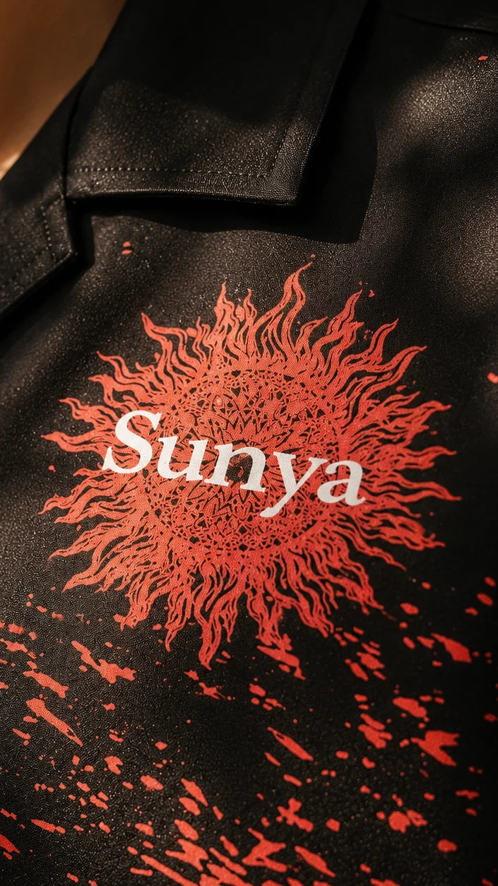 Close-up of the red Sunya sun emblem and splatter print on the black BLAZE shirt