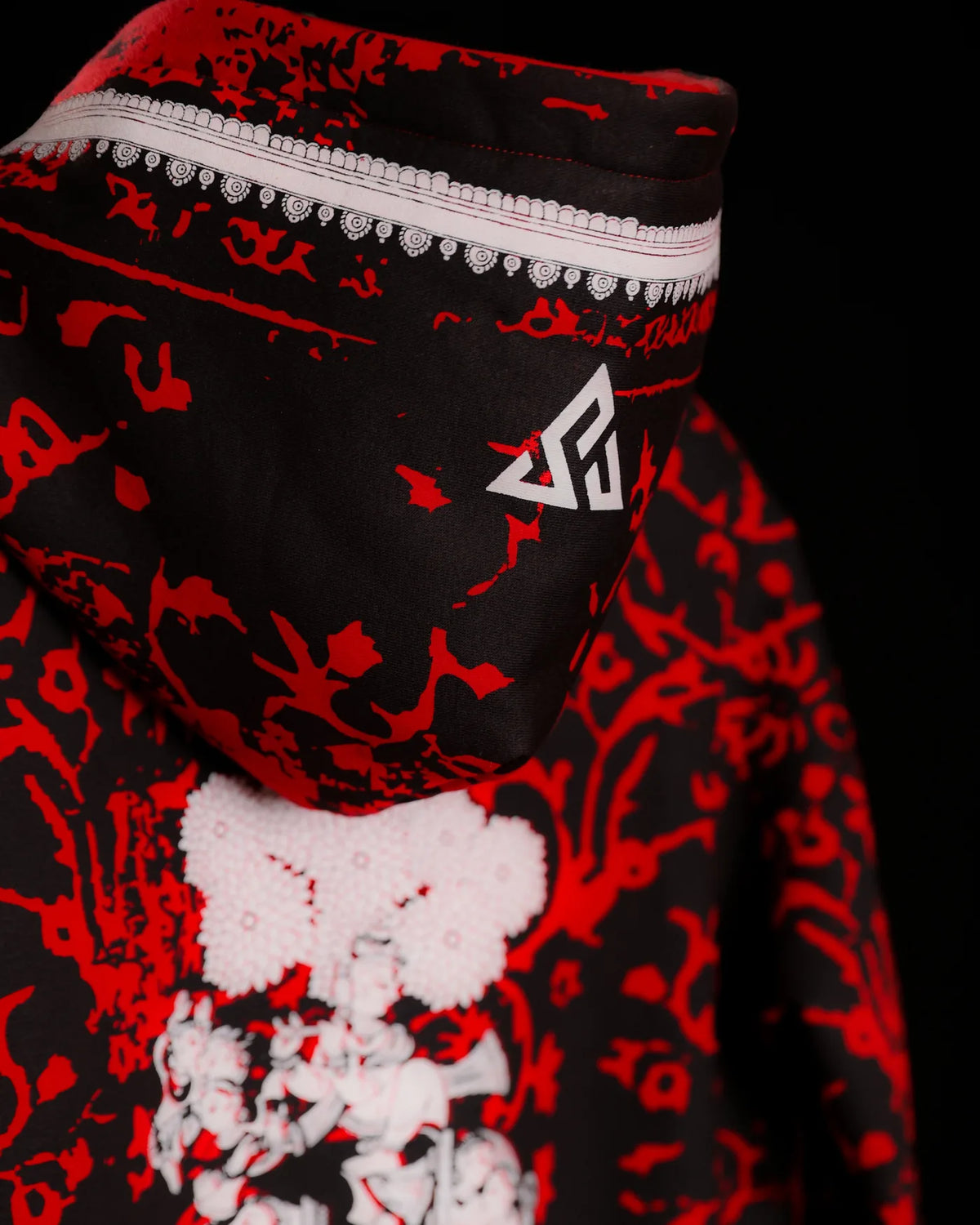 The back of the ĀRAMBH hoodie: red floral vine on black, the white Sunya emblem on the hood and the figural illustration below