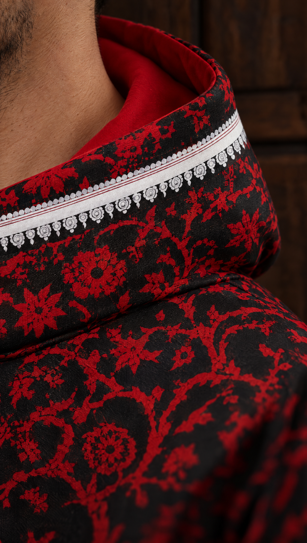 The white scalloped trim along the hood of the red and black ĀRAMBH hoodie