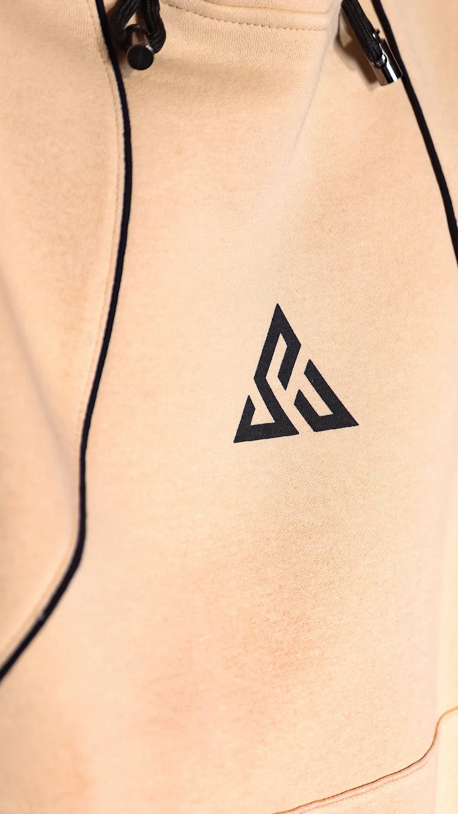 The sand FUSION hoodie: black contrast piping curving past the Sunya emblem and the hood toggles