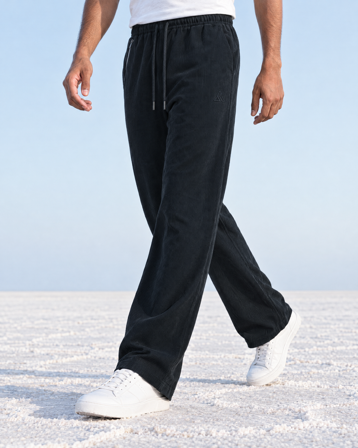 Mid-stride on the salt flats in the BHASMA cord joggers in near-black charcoal, the straight leg falling open to the ankle
