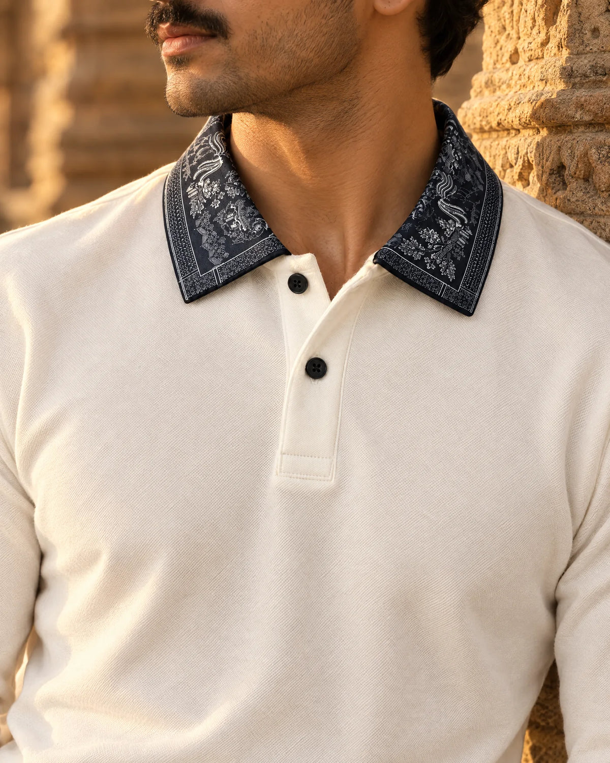 Close-up of the cream Full Sleeve Oxford Polo on body, its navy printed collar lit by low sun against a sandstone pillar
