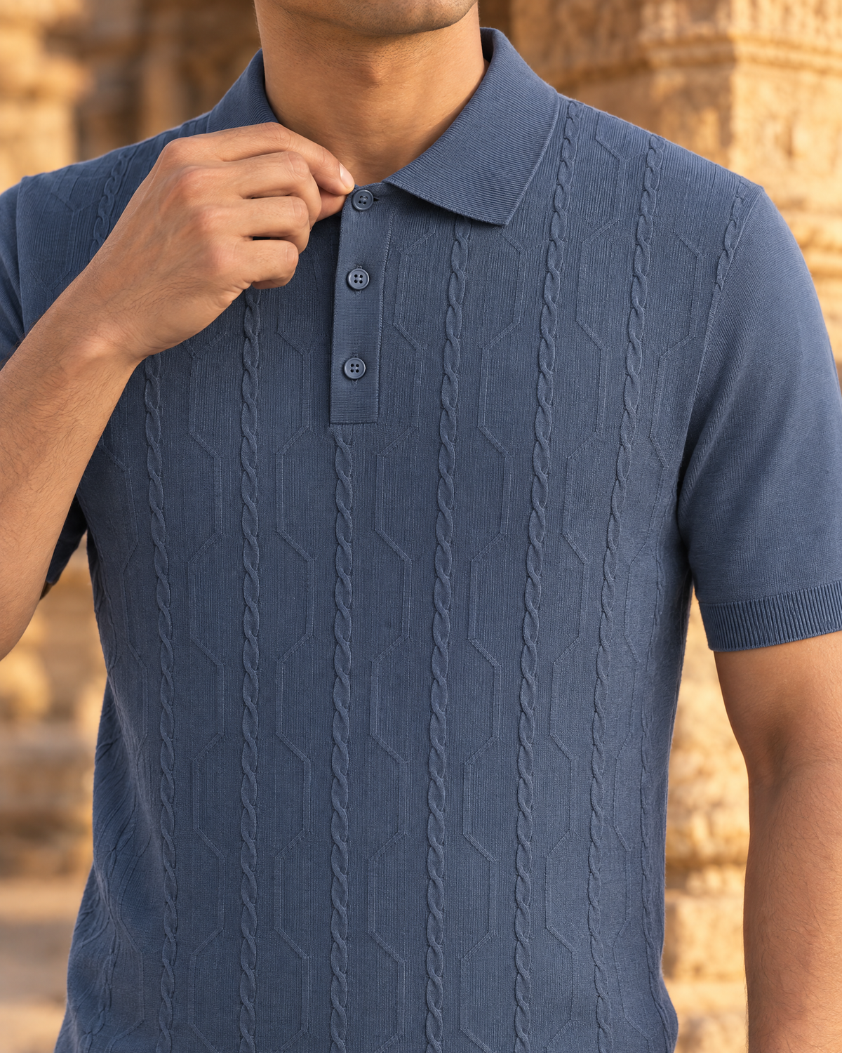 A hand fastening the top button of the slate VANE knit polo