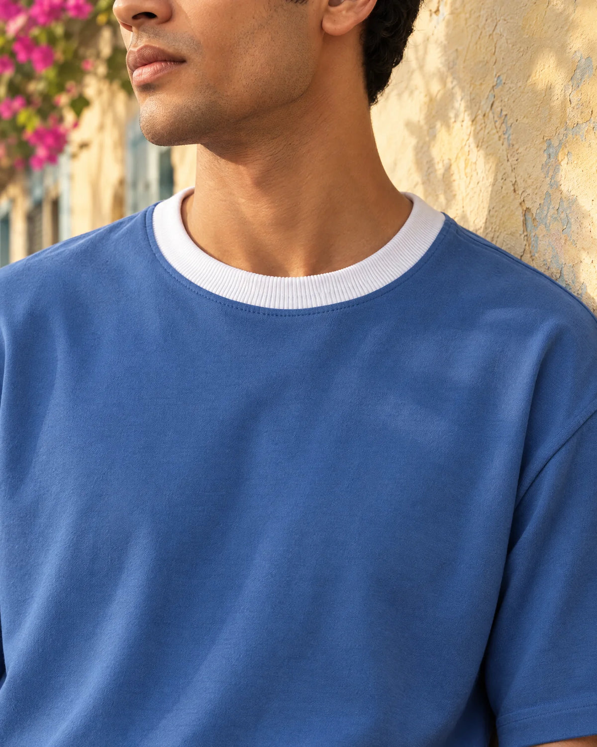 Close-up of a royal-blue tee with a white rib collar against a sunlit Bandra cottage wall