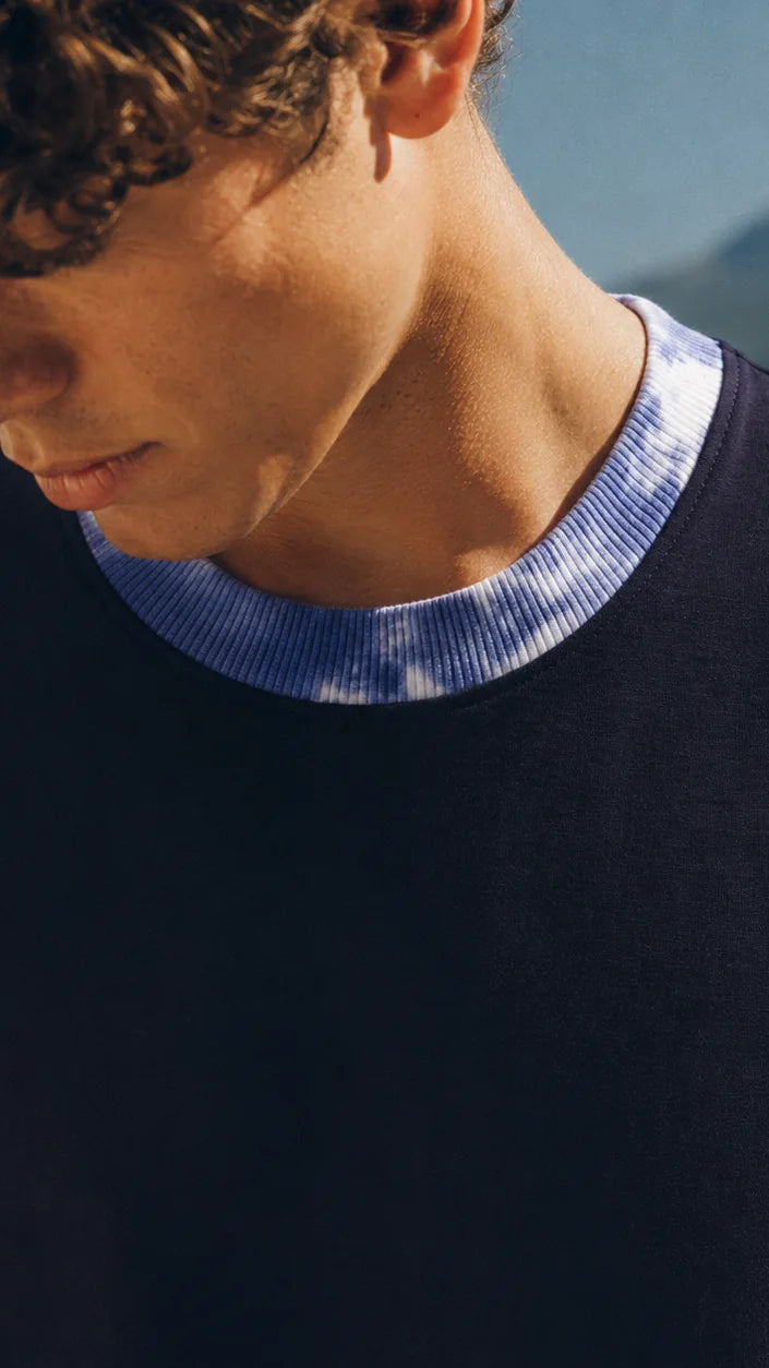 Close-up of the blue-and-white tie-dye rib collar on a navy tee