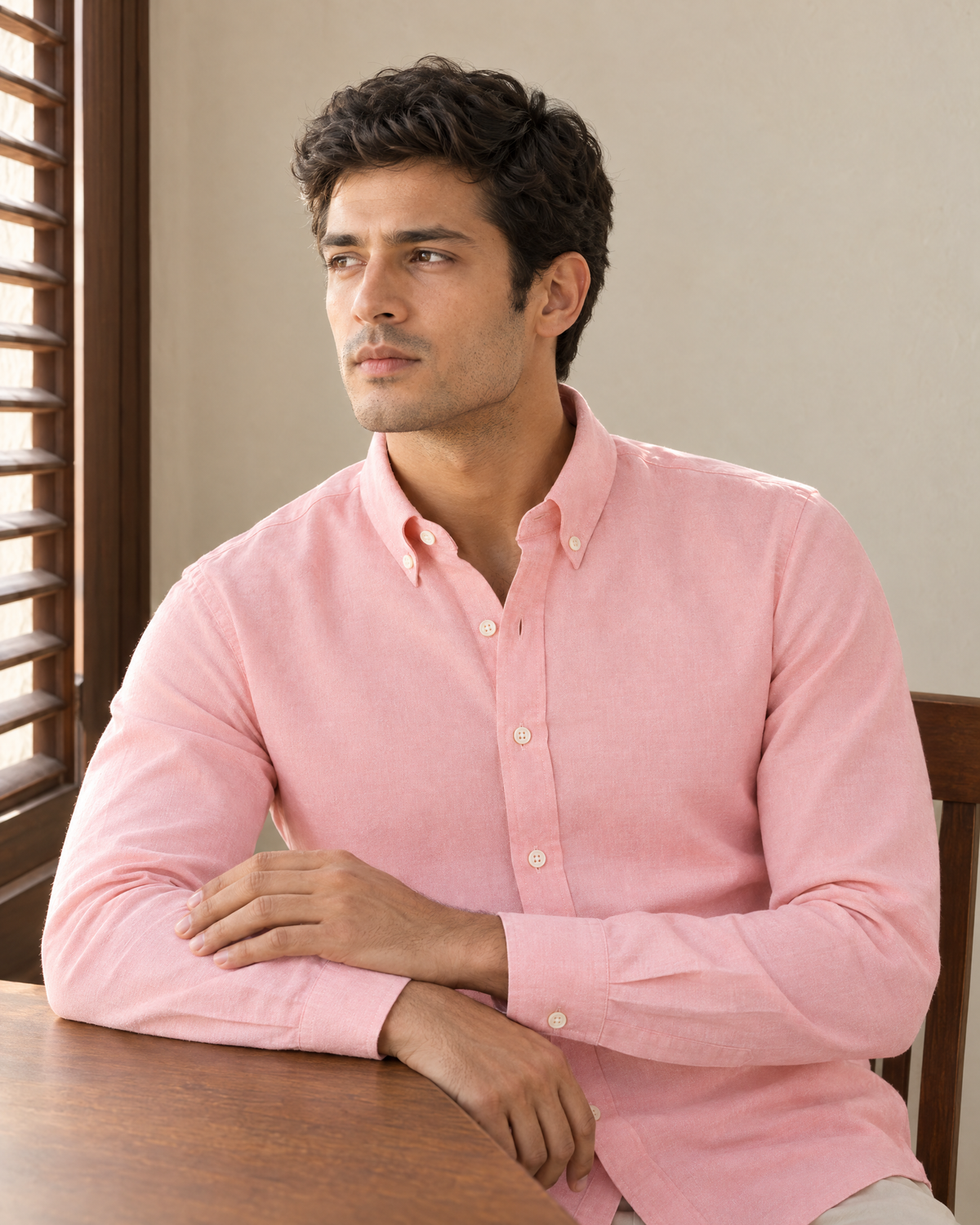 A man in the Blush Oxford Shirt seated at a teak desk beside a shuttered window