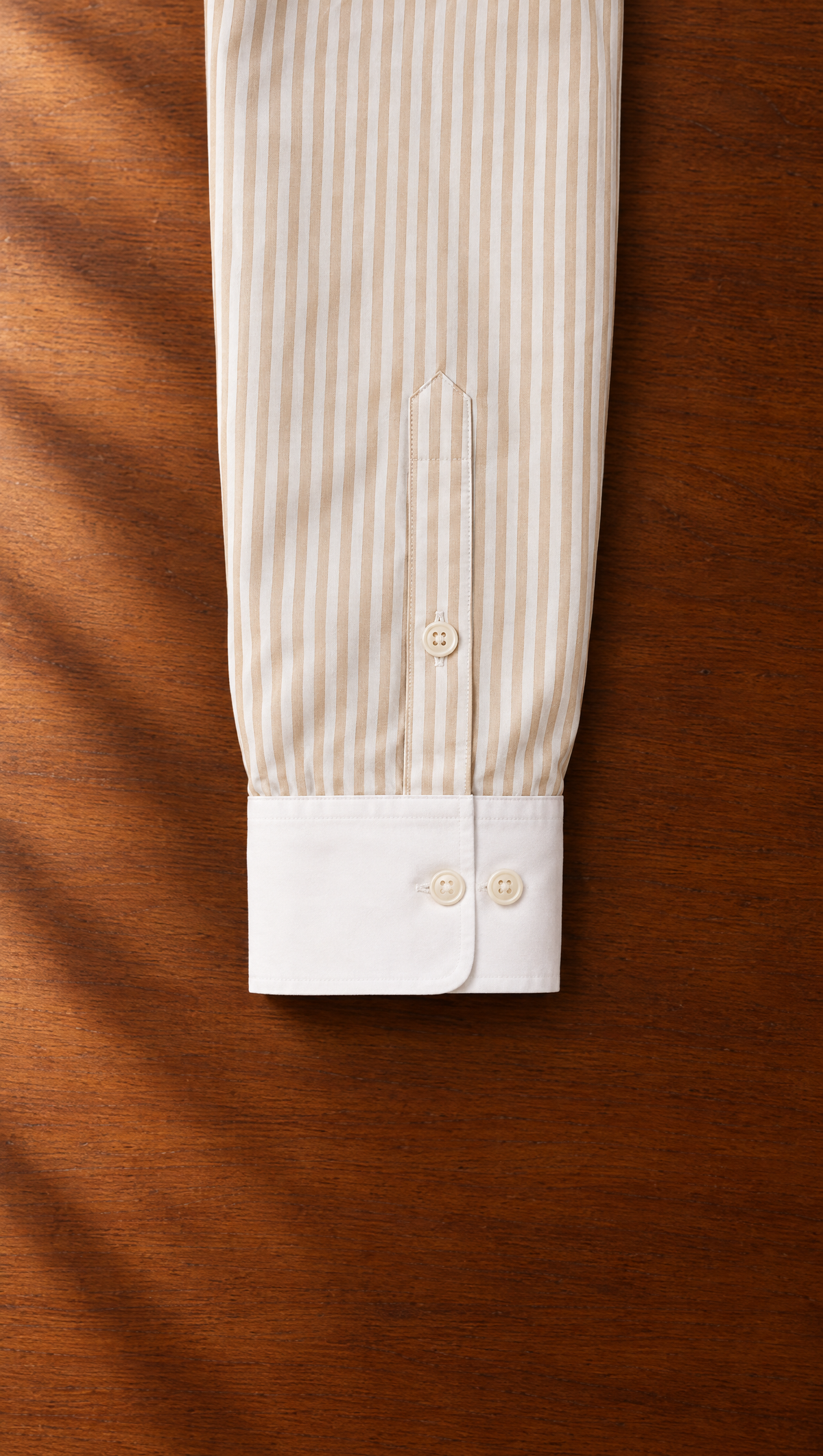 The Sand Stripe Shirt's solid white two-button cuff laid on a teak desk