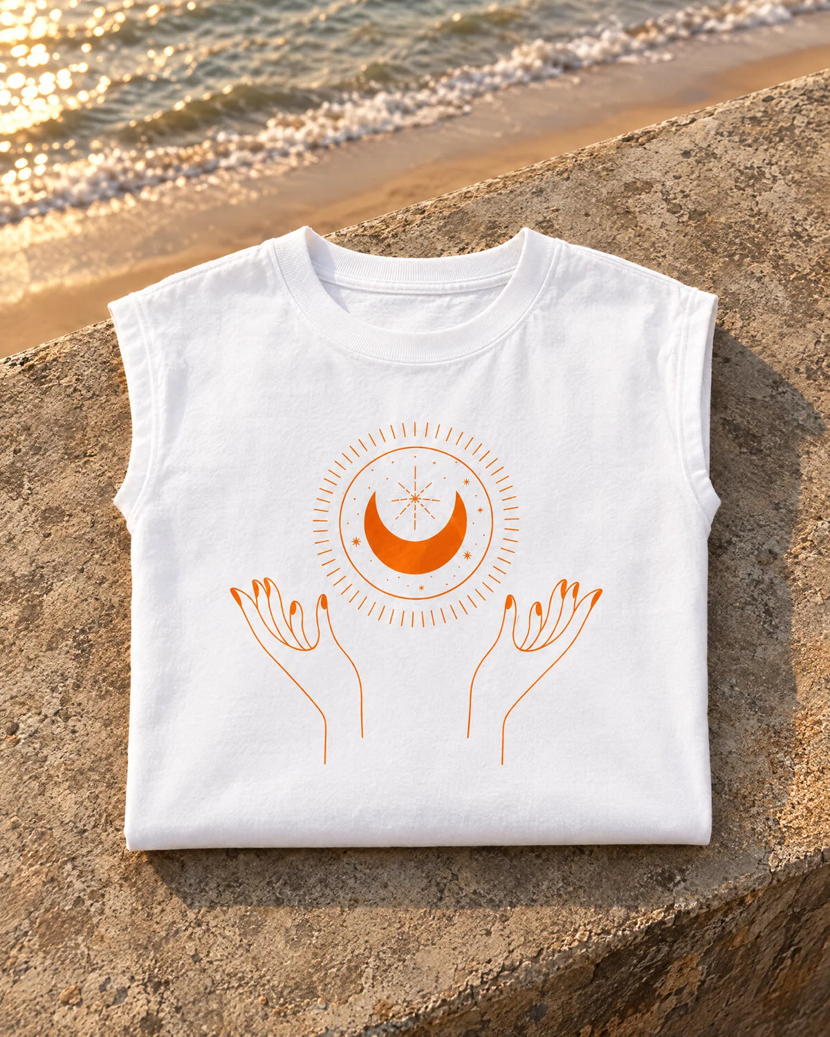 White sleeveless tee folded on a sun-warmed Juhu sea-wall ledge, orange sun, moon and hands print facing up