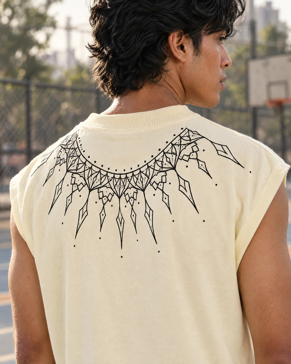 Back view of a man on a basketball court wearing a cream sleeveless tee with a black sunburst arc across the upper back