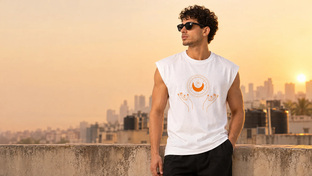 Man in a white sleeveless tee with an orange sun, moon and open-hands print on a Mumbai rooftop at golden hour