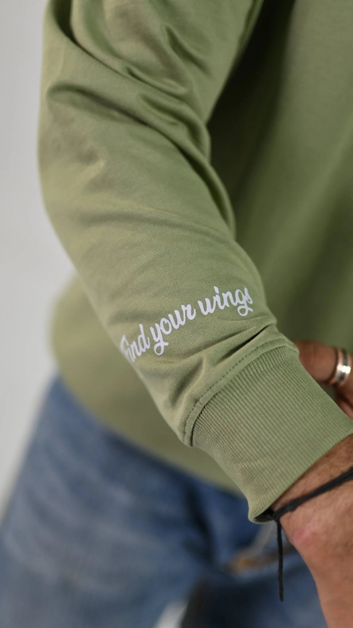 Close-up of the white 'Find your wings' script above the ribbed cuff on the sage-green Rebirth Phoenix sleeve