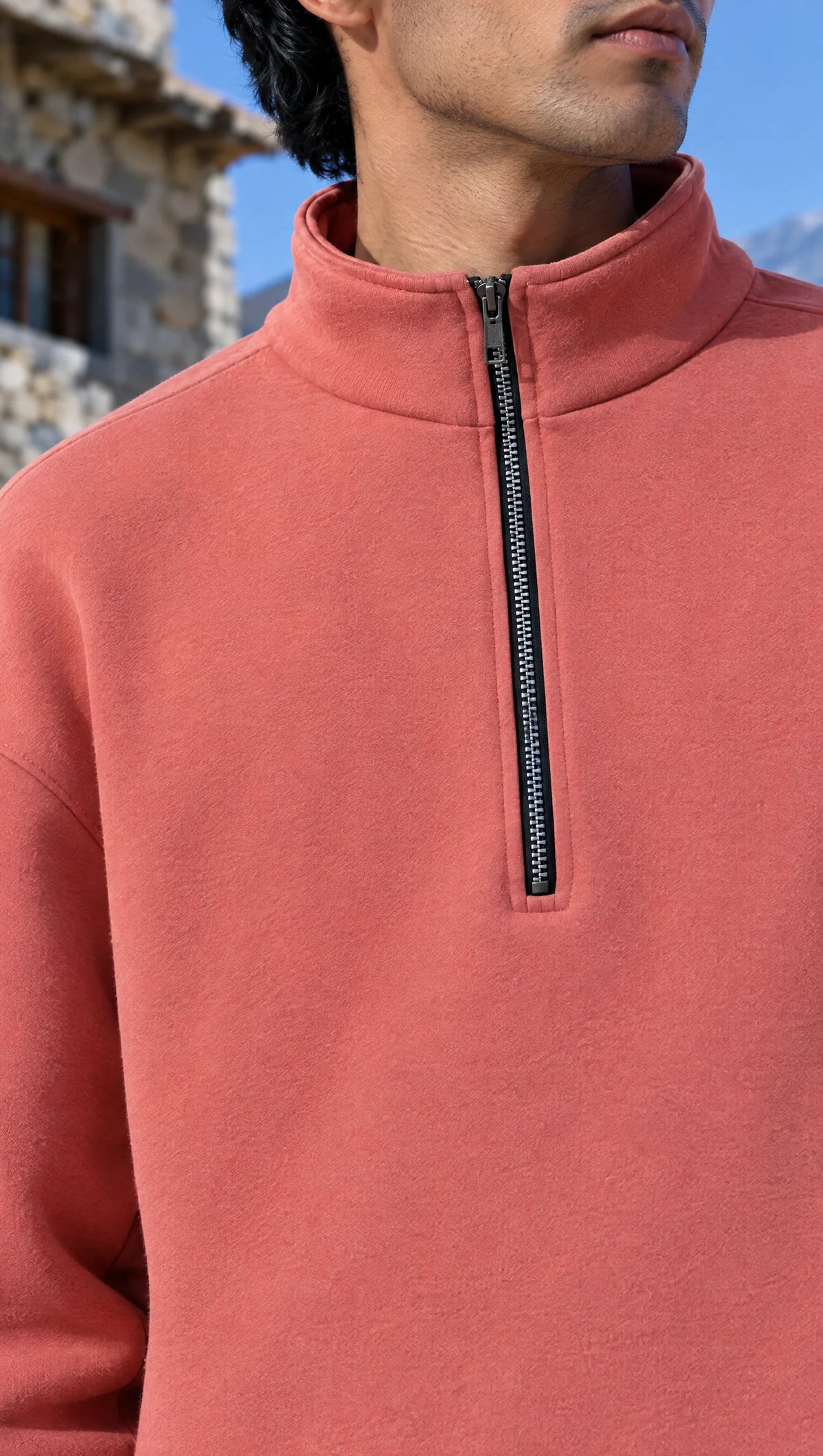 Close-up of the funnel collar and metal quarter-zip on the coral HAVEN fleece sweatshirt, stone homestay behind