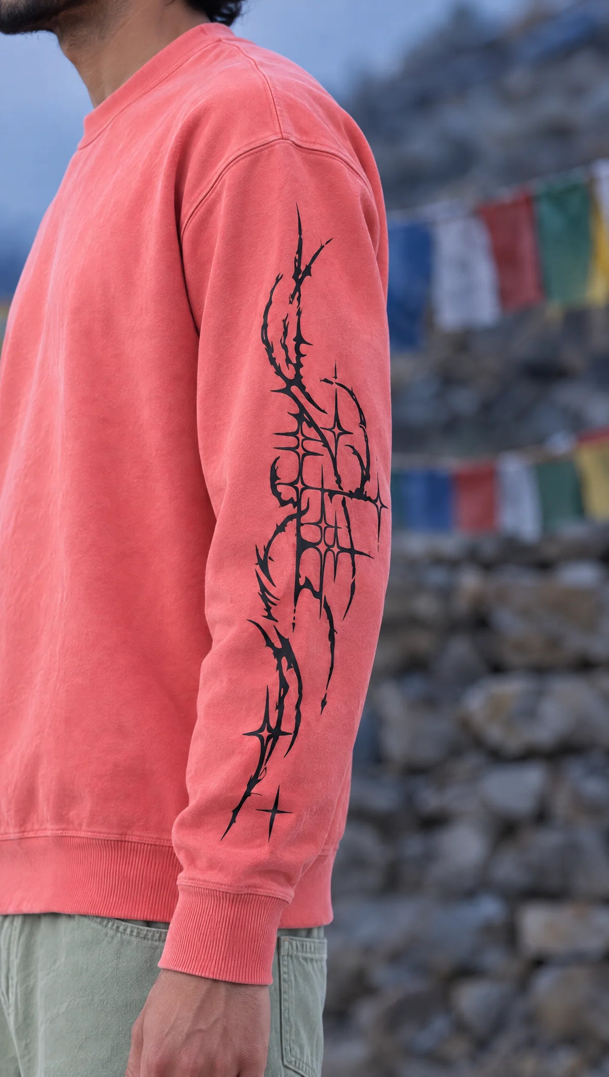 Close-up of the black thorn linework running down the sleeve of the Tragic Bloom sweatshirt, prayer flags blurred behind