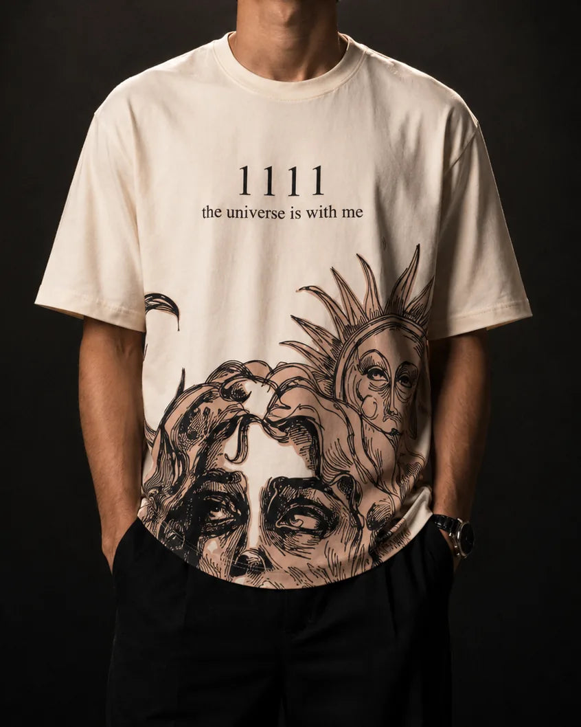 The bone-white Manifest tee worn: 1111 and “the universe is with me” at the chest, a sun and a classical face in line art down to the hem