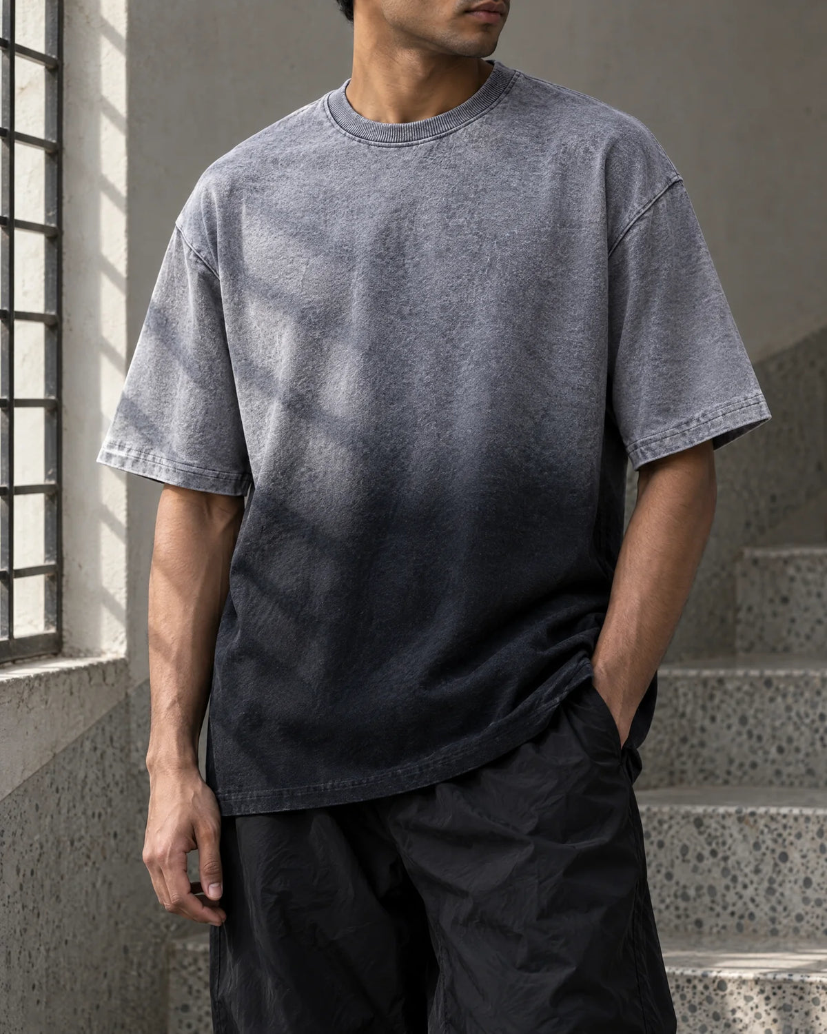 Torso detail of an oversized tee fading from ash-grey to charcoal-black in a terrazzo stairwell